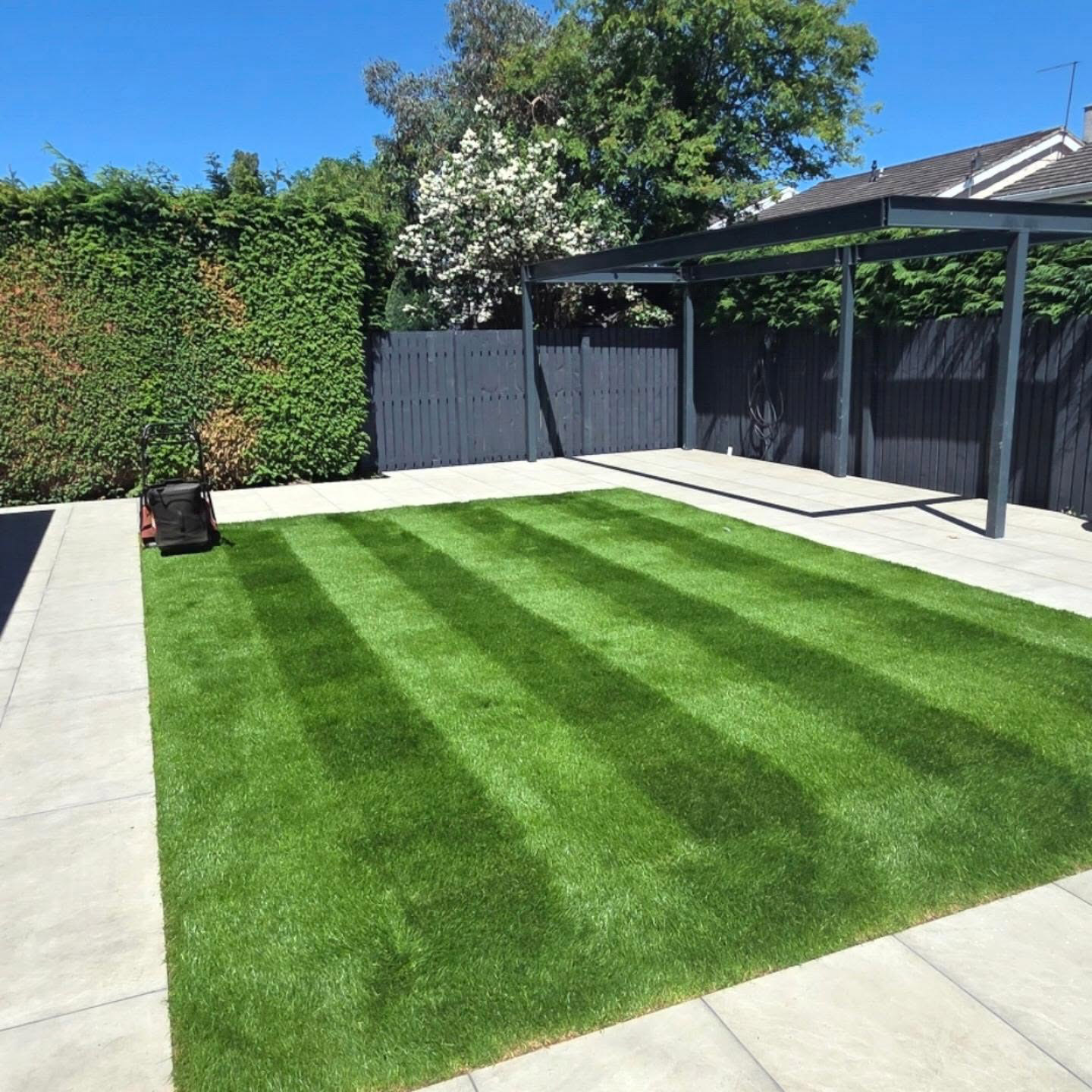 Striped lawn bordered by a light stone patio